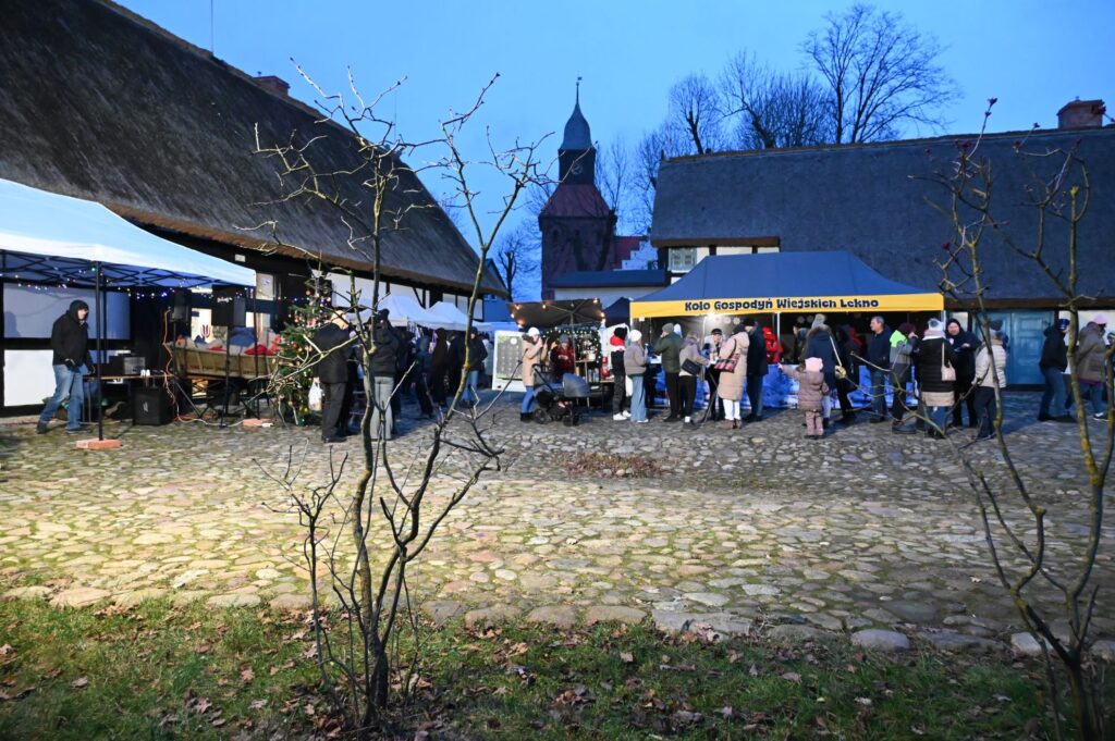 Widok na jarmark o zmierzchu, z oświetlonymi stoiskami i odwiedzającymi na placu (kliknięcie powiększy zdjęcie).
