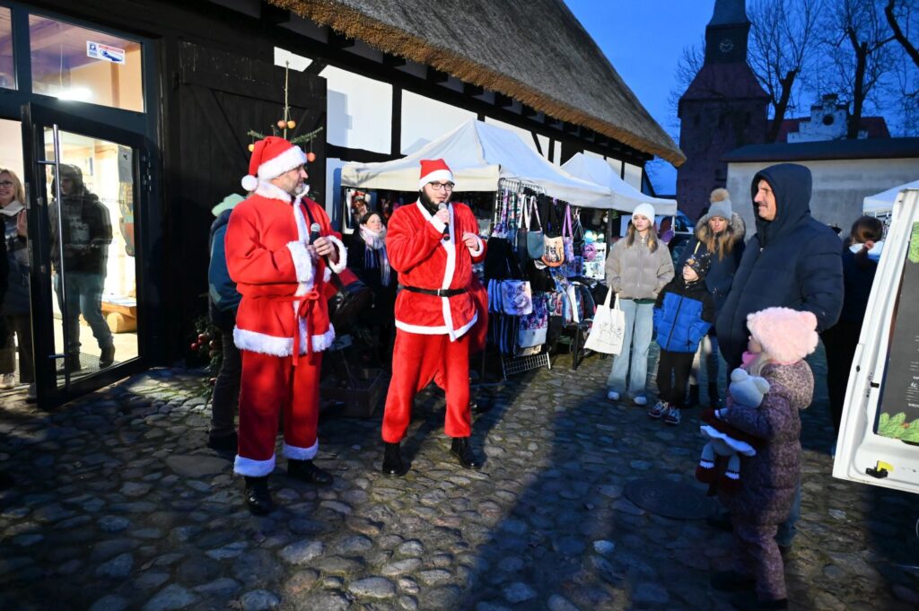 Mikołaje stoją przed budynkiem i rozmawiają z dziećmi oraz dorosłymi podczas wydarzenia (kliknięcie powiększy zdjęcie).