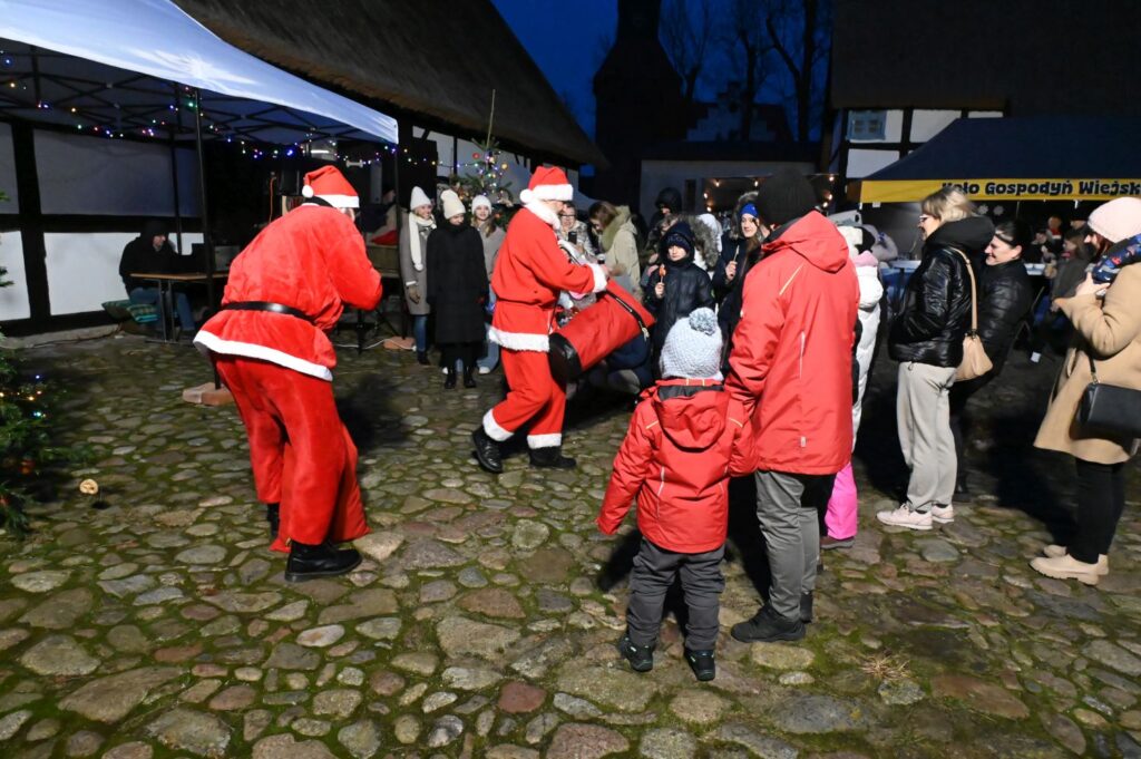 Mikołaj rozdaje upominki dzieciom, a wokół stoją uczestnicy jarmarku (kliknięcie powiększy zdjęcie).
