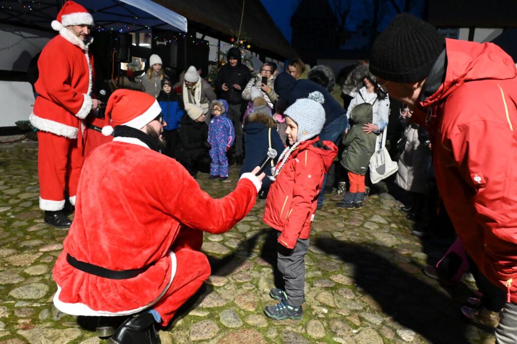 Mikołaj kuca i wręcza dziecku drobny upominek w obecności innych uczestników (kliknięcie powiększy zdjęcie).