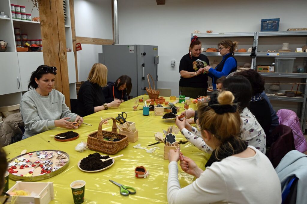 Grupa dorosłych uczestniczy w warsztatach plastycznych, przygotowując dekoracje wielkanocne (kliknięcie powiększy zdjęcie).