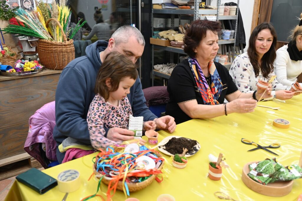Uczestnicy warsztatów rękodzielniczych tworzą ozdoby przy wspólnym stole (kliknięcie powiększy zdjęcie).