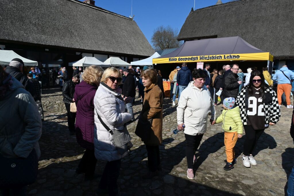 Tłum odwiedzających spaceruje między stoiskami na dziedzińcu zagrody podczas jarmarku (kliknięcie powiększy zdjęcie).