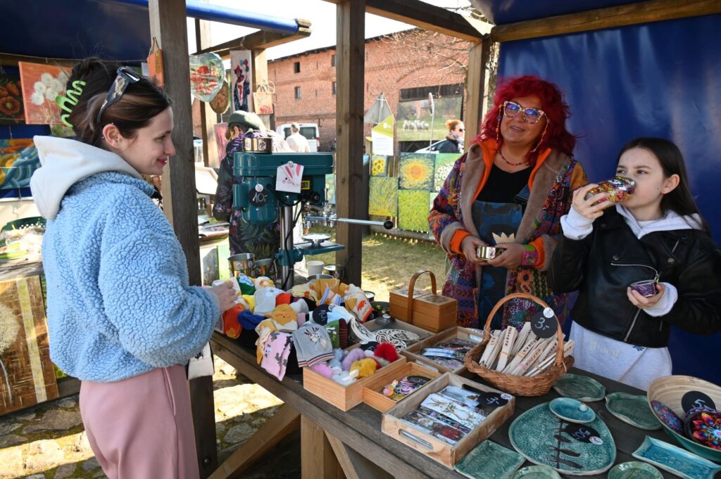 Sprzedawczyni rozmawia z klientką przy stoisku z rękodziełem podczas jarmarku (kliknięcie powiększy zdjęcie).