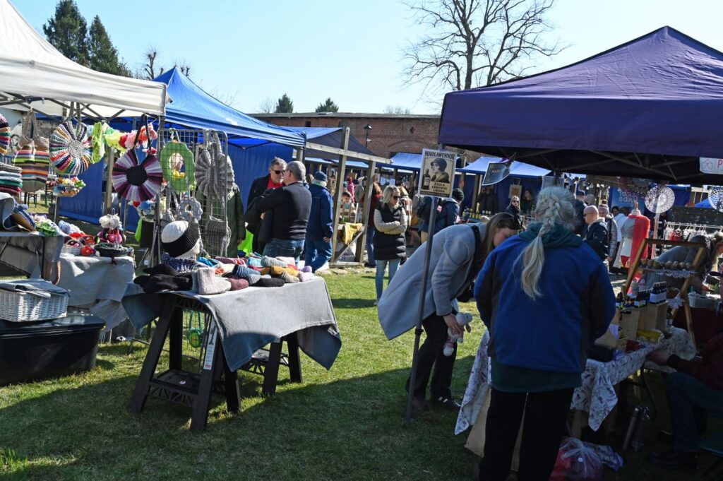 Stoiska z rękodziełem i dekoracjami ustawione na trawie, odwiedzający oglądają produkty podczas jarmarku (kliknięcie powiększy zdjęcie).