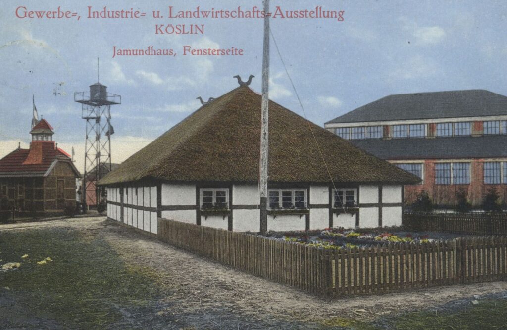 Rekonstrukcja jamneńskiej chaty o konstrukcji szachulcowej i dachu krytym strzechą prezentowana na wystawie przemysłowo-rolniczej w Koszalinie w 1912 roku, z ogrodzeniem i rabatą kwiatów przed budynkiem (kliknięcie powiększy zdjęcie).