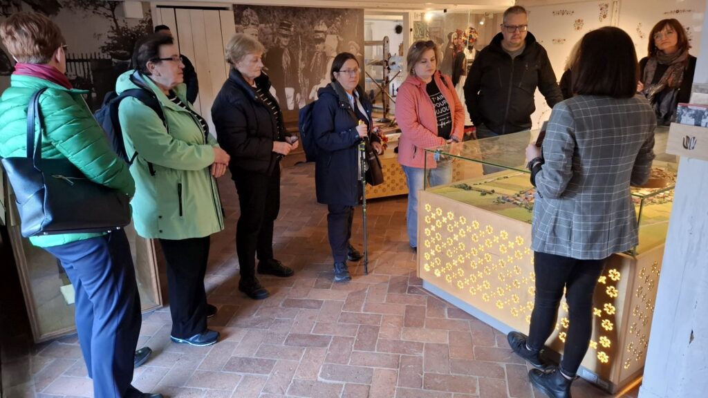 Grupa zwiedzających stoi wokół podświetlanej gabloty z makietą, słuchając przewodniczki opowiadającej o ekspozycji (kliknięcie powiększy zdjęcie).