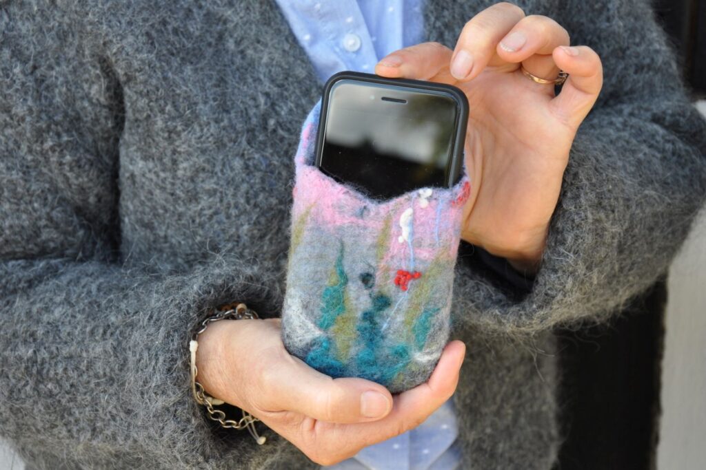 Ręce uczestniczki prezentujące filcowane etui na telefon w pastelowych kolorach z włożonym smartfonem (kliknięcie powiększy zdjęcie).