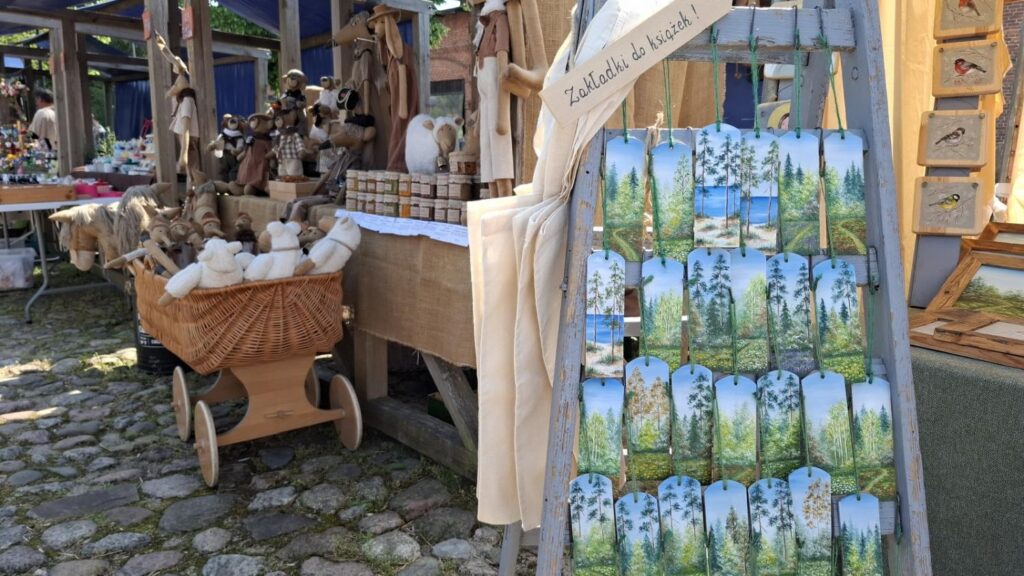 Stoisko z drewnianymi wyrobami i tekstyliami. Na ekspozytorze zawieszono torby z nadrukami przedstawiającymi leśne krajobrazy. (kliknięcie powiększy zdjęcie).