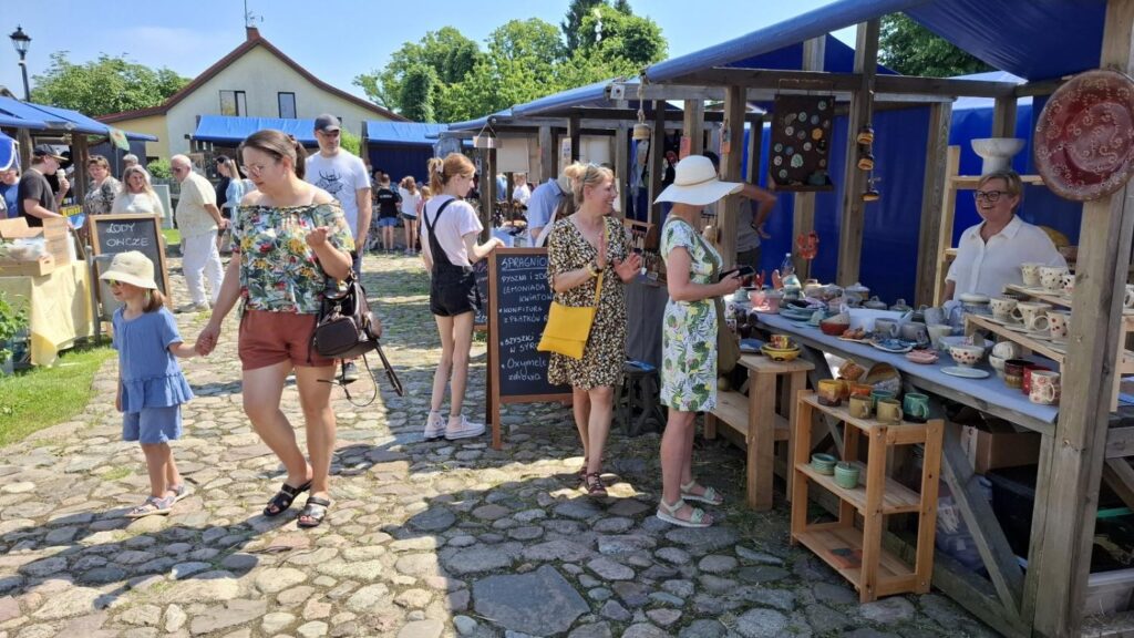 Odwiedzający spacerują między stoiskami jarmarku, zatrzymując się przy ekspozycji ceramiki i rękodzieła. (kliknięcie powiększy zdjęcie).