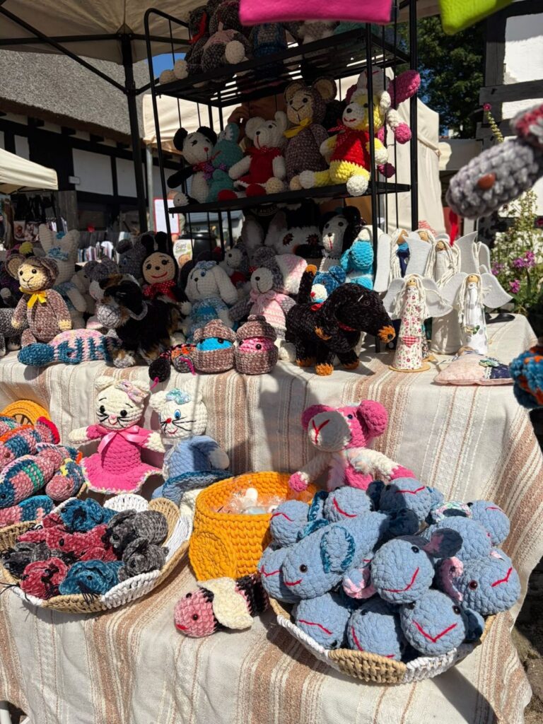 Stoisko z kolorowymi, szydełkowanymi maskotkami; na półkach i stole znajdują się między innymi misie, koty, psy, słonie i aniołki (kliknięcie powiększy zdjęcie).